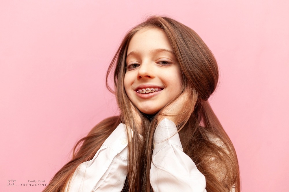 Confident young woman posing against a pink background, smiling naturally after orthodontic braces for overbite in chester springs, pa.